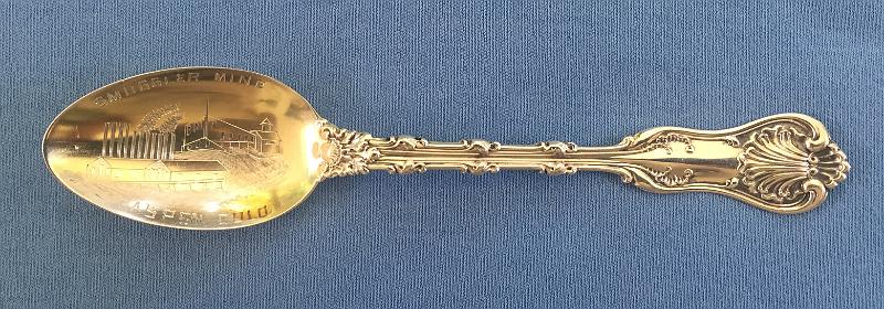 Souvenir Mining Spoon Smuggler Mine Aspen.JPG - SOUVENIR MINING SPOON SMUGGLER MINE ASPEN CO - Sterling silver souvenir spoon, 5 1/4 in. long, bowl engraved with mine and mill buildings and marked SMUGGLER MINE ASPEN COLO, handle marked in decorative pattern,  reverse marked Sterling with maker’s mark for Whiting Manufacturing Co. (1866-1926 New York City) and Pat. 1893 [The Smuggler Mine is located on the slopes of Smuggler Mountain, at the north edge of Aspen, Colorado. It is the oldest operating silver mine in the Aspen mining district.  The name Smuggler came from Charles Bennett, the first recorded claimant, in 1879.  Bennett added to his mining claims a ranch in the area of the valley floor being used as a camp. In 1880 he sold them all to B. Clark Wheeler and Charles Hallam, who with their partners, among them David Hyman, the Cincinnati man who had first hired them to search for business opportunities in Colorado, formed the Aspen Town and Land Company. They surveyed and platted the 282-acre ranch, subdivided it, named the streets after themselves and sold the lots for $10 each, an event which brought the city of Aspen into existence.  Hyman eventually assumed control of the Smuggler Mine which became wildly productive in the late 1880s.  The passage of the Sherman Silver Purchase Act in 1890, increasing the federal government's required purchase of that metal, contributed considerably to the prosperity of the city, whose population reached its all-time peak that year of over 10,000.  For a time in the early 1890s, the Smuggler employed over 200 miners and produced one-fifth of the world’s silver.  With the repeal of the Sherman Silver Purchase Act in 1893, the price dropped, and many of Aspen's mines had to close.  The Smuggler ceased most operations and laid off 70 of its miners.  In 1894 the largest silver nugget ever was mined from Smuggler's depths. Originally, it weighed 2,340 pounds, but was too large to be brought from the mine intact. It was broken into three pieces, the largest weighing 1,840 pounds. The price of silver began to rise slightly in 1895, and the Smuggler was one of the few mines in the Aspen area to reopen. In 1917 the Smuggler reached the bottom of the vein that had been the mine's main source of ore and David Hyman decided to shut down the mine. The mine opened briefly in the 1970s but in 1984 it was designated a Superfund site after tests found high levels of lead and cadmium in the soil. It took the Environmental Protection Agency 12 years to clean up the site. While it is estimated that nearly a million pounds of recoverable ore remain in the mine, it is used as much for tours today as mining. In 2015 the mine, now listed on the National Historic Register, was sold and continues as an underground tour attraction.]